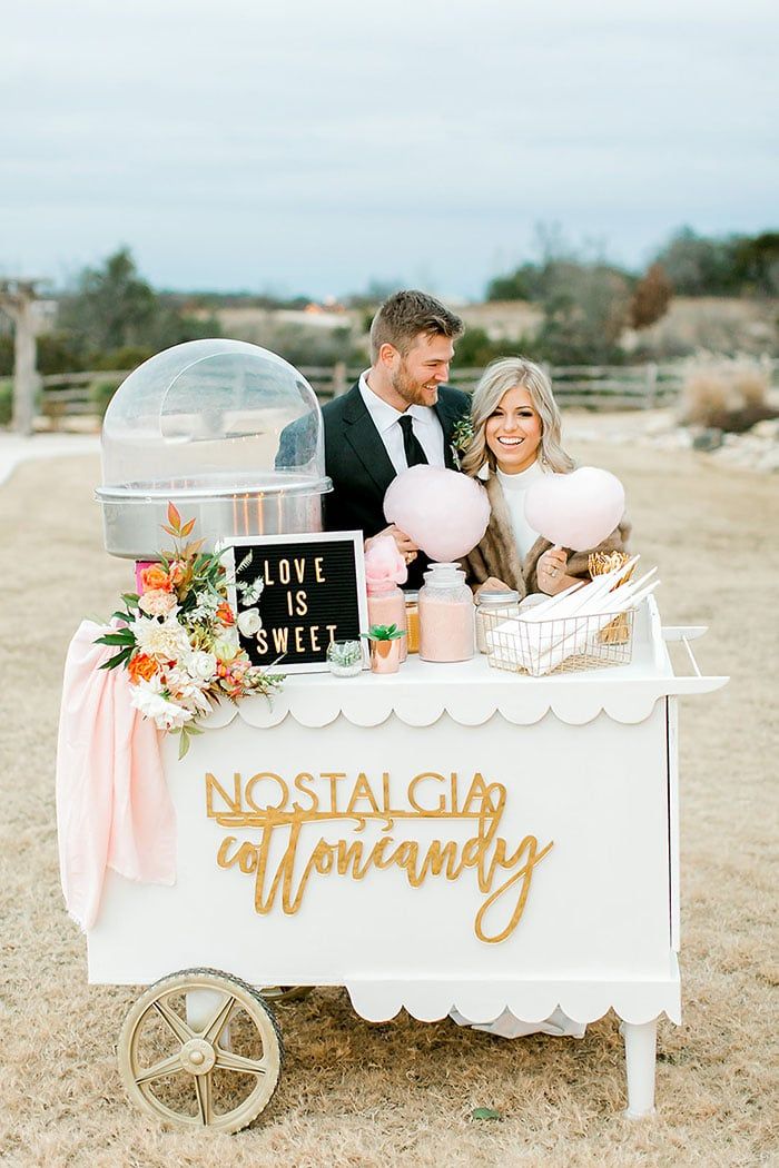 a man and woman standing behind a white cart with pink balloons on the side, in front of a sign that says love is sweet