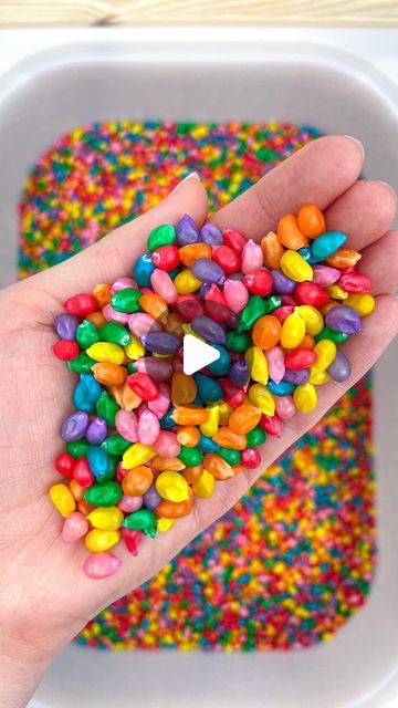 a hand holding a handful of candy sprinkles in front of a white bowl