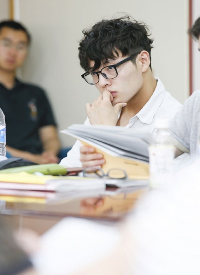 two men sitting at a table with papers and water bottles in front of them,