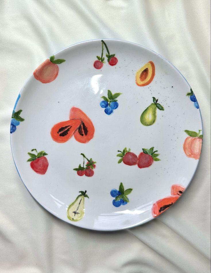 a plate with fruit painted on it sitting on a white cloth covered tablecloths