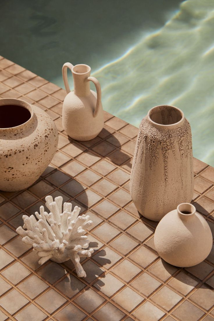 three white vases sitting on top of a tiled floor next to a swimming pool