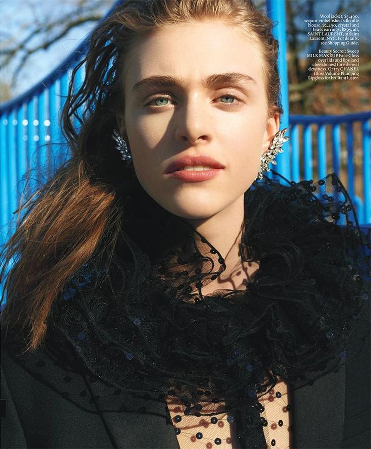 a young woman with long hair wearing a black jacket and polka dot shirt, standing in front of a blue fence