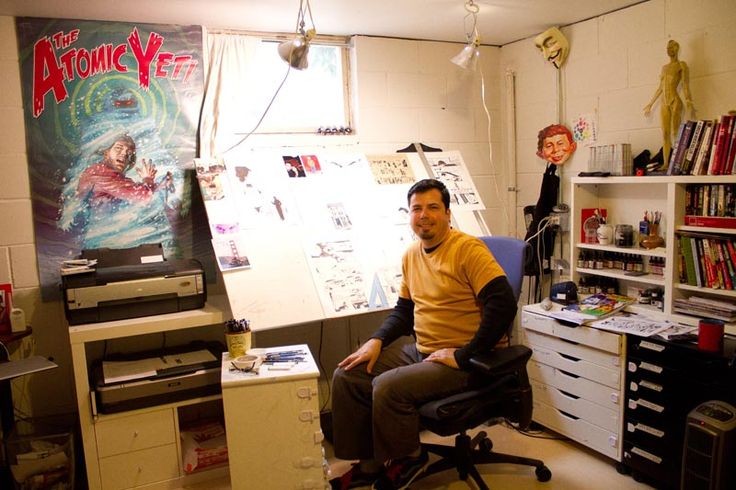 a man sitting in an office chair next to a desk and shelves with books on it