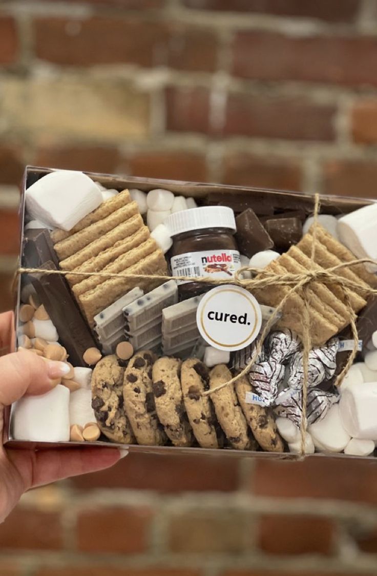 a person holding up a box filled with cookies and marshmallows