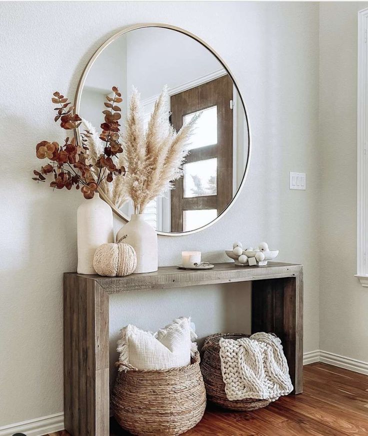 a wooden table topped with a round mirror next to a vase filled with dried flowers