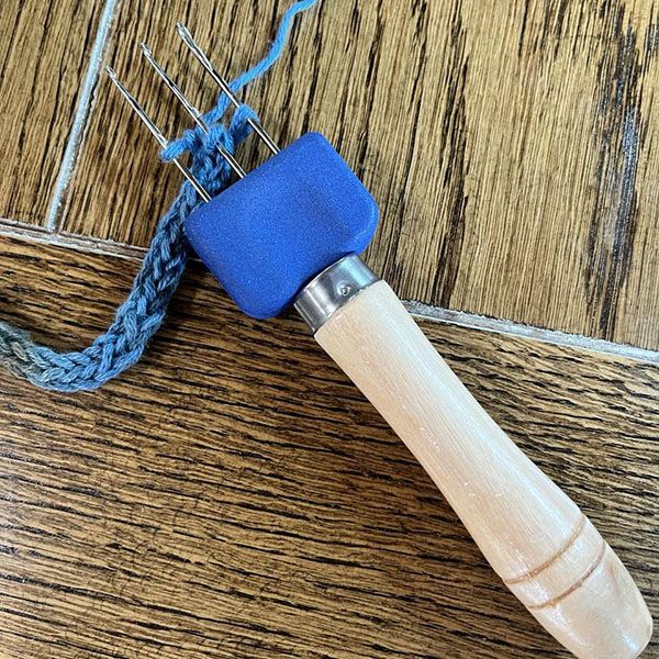 a blue piece of wood sitting on top of a wooden table next to a metal pin