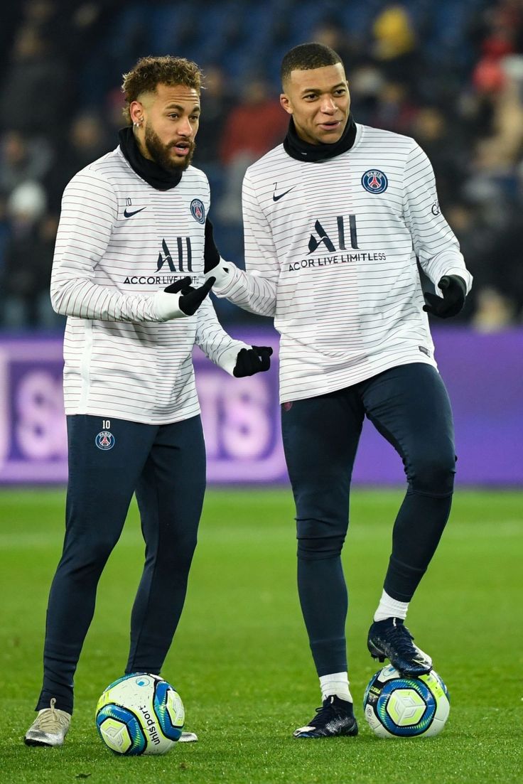 two soccer players standing next to each other on a field with balls in their hands