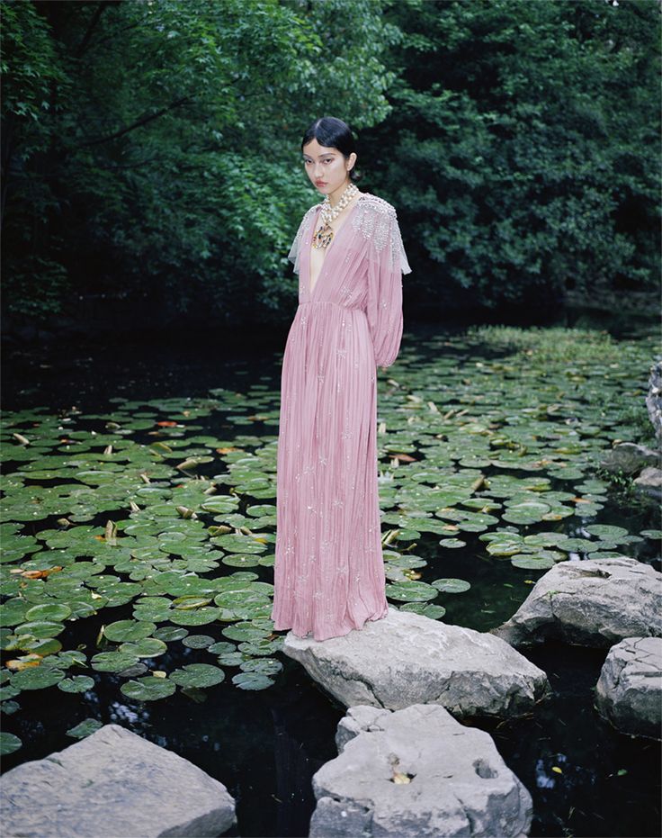 a woman in a pink dress standing on rocks near water lillies and lily pads