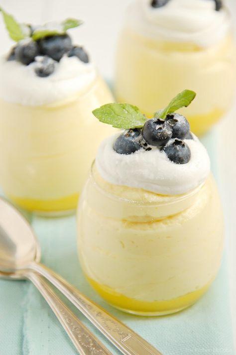 three desserts with blueberries and whipped cream in small glass jars on a table