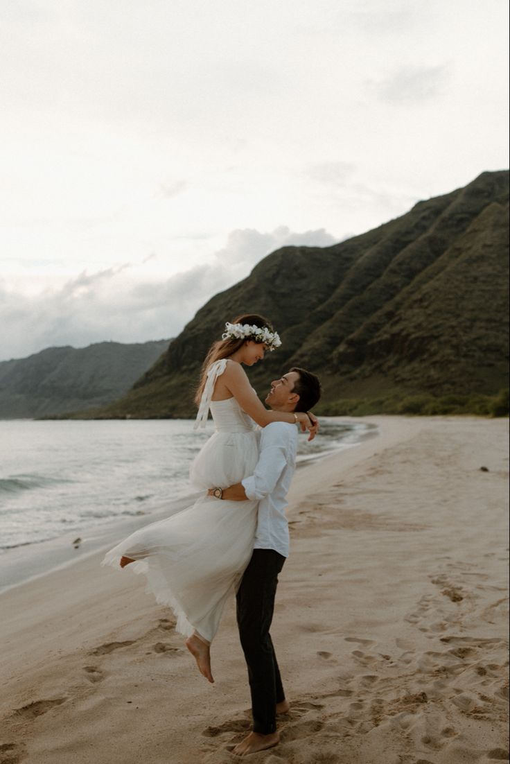 a man and woman are standing on the beach with their arms around each other as they dance