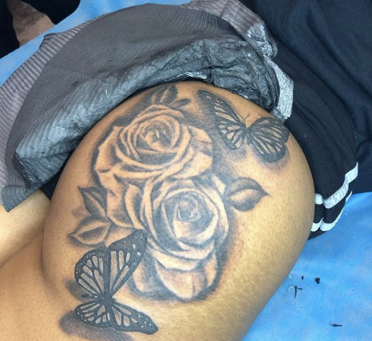 a woman's thigh with a rose and butterflies tattoo on it, sitting on a bed