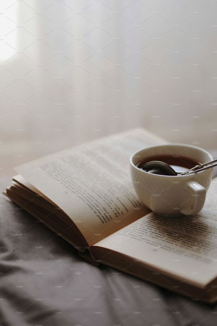 an open book with a cup of coffee on top of it next to a spoon