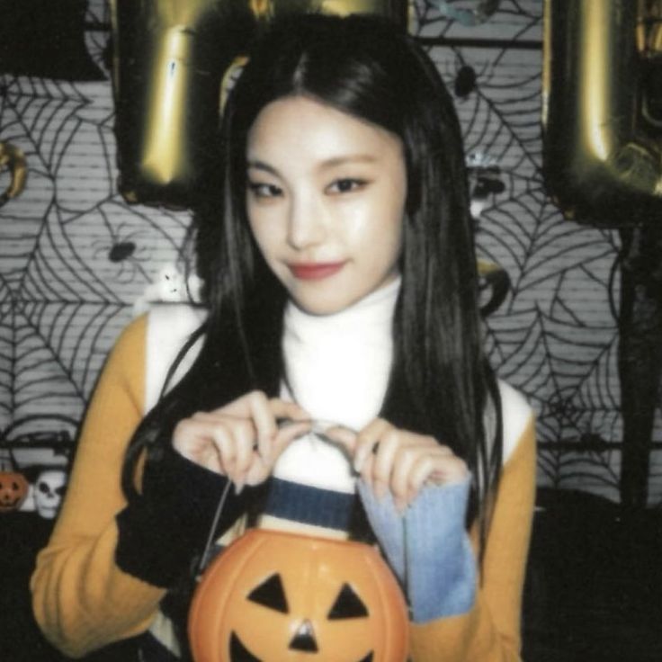 a young woman holding a jack - o'- lantern in front of her face