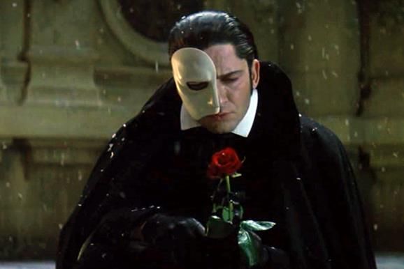 a man with a mask on holding a rose in his hand and looking down at the ground