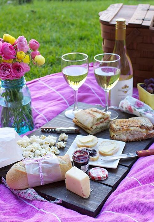 a picnic with wine, cheese and crackers on a blanket next to flowers in a vase