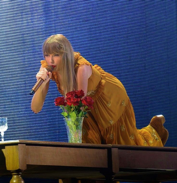 a woman in a yellow dress leaning over a table with a vase full of flowers