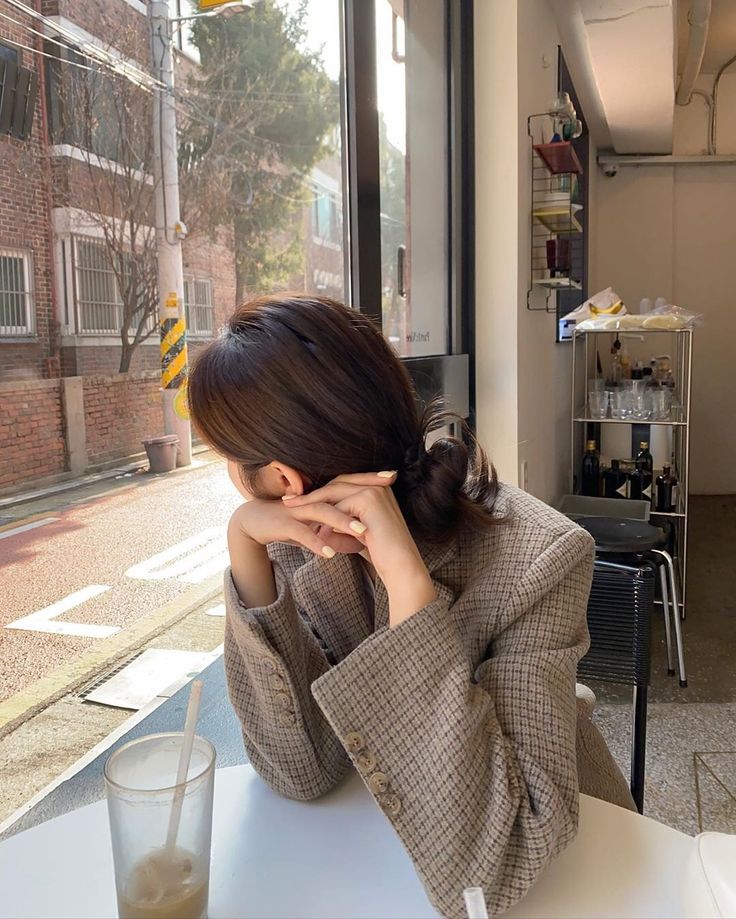 a woman sitting at a table in front of a window with her hand on her face