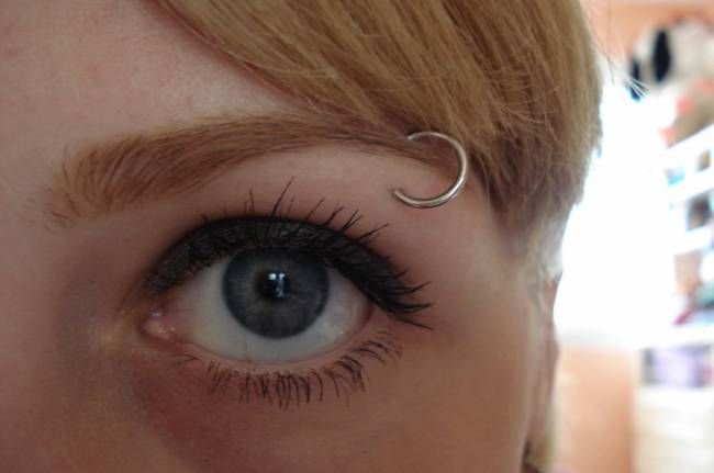 a close up of a woman's eye with long eyelashes and piercing on her nose