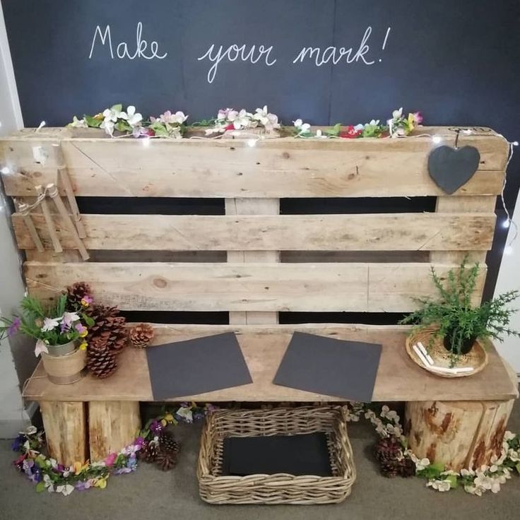 a wooden bench made out of pallets with flowers and plants on it, next to a chalkboard that says make your mark