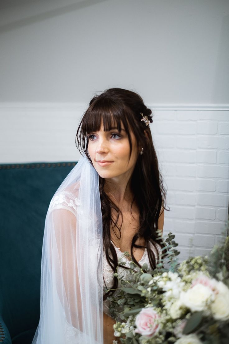 a woman wearing a veil and holding a bouquet in her hand while sitting on a couch