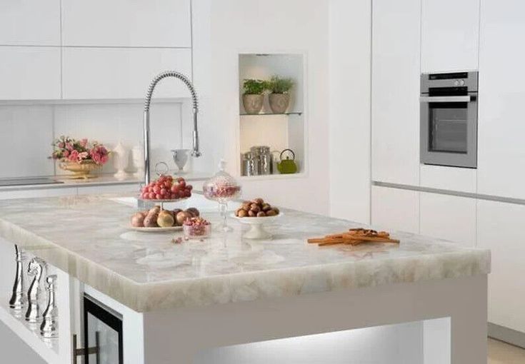 a white kitchen with marble counter tops and stainless steel appliances, along with an island in the middle