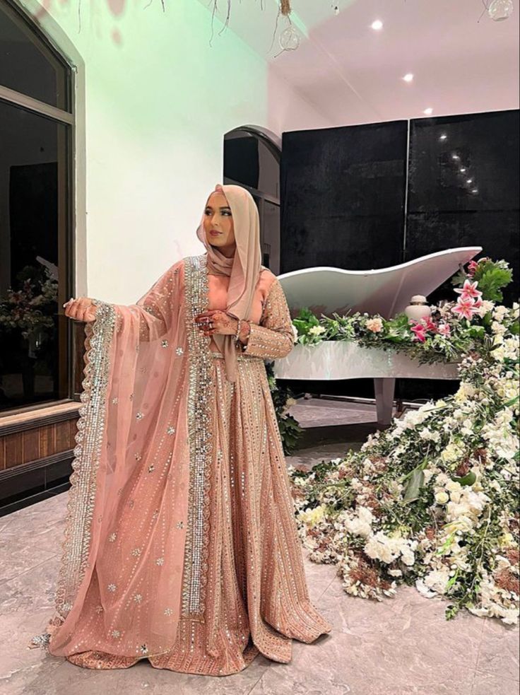 a woman in a hijab standing next to a flower arrangement and looking at the camera