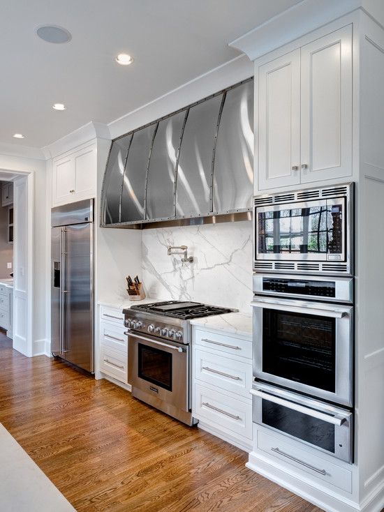 a kitchen with white cabinets and stainless steel ovens, wood flooring and hardwood floors