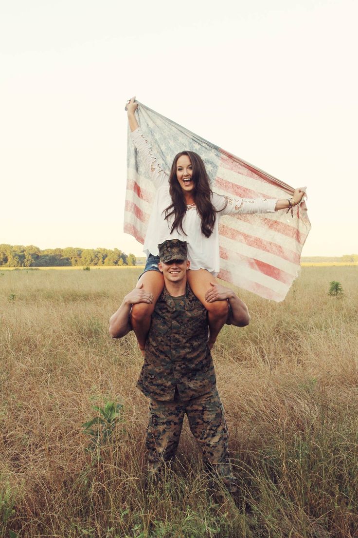 a man carrying a woman on his back while standing in a field with an american flag