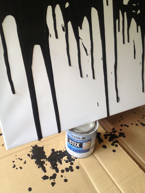 a can of paint sitting on top of a table next to a wall with black and white dripping paint