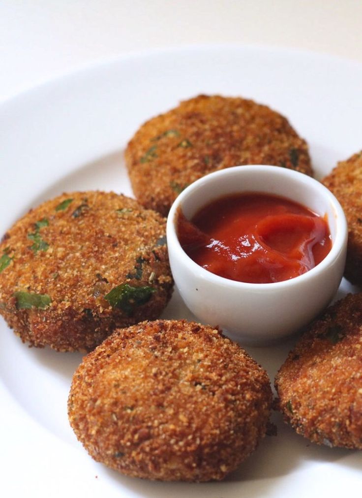 some fried food on a white plate with ketchup in a small bowl next to it