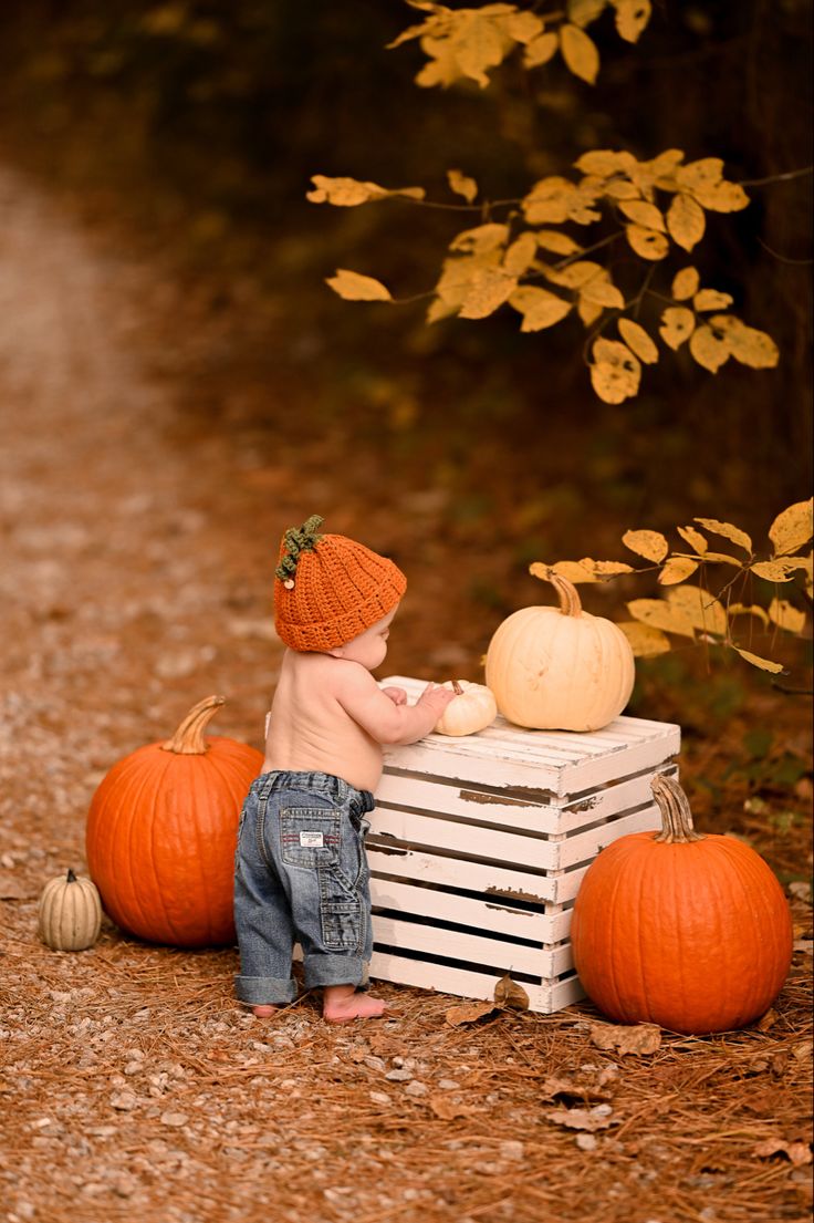 a baby sitting on top of a crate next to pumpkins