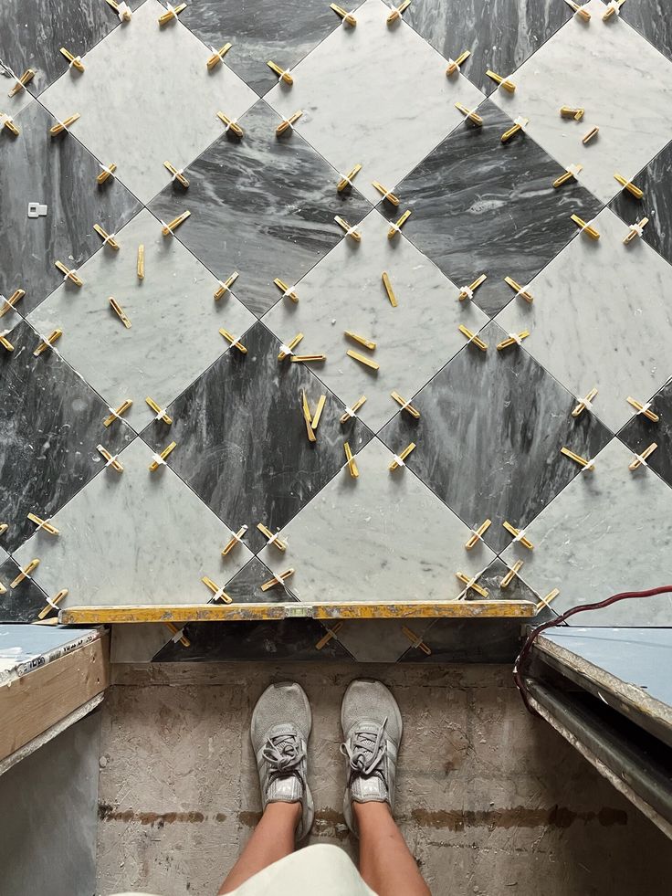 someone's feet on the ground in front of a tiled wall with crosses and nails