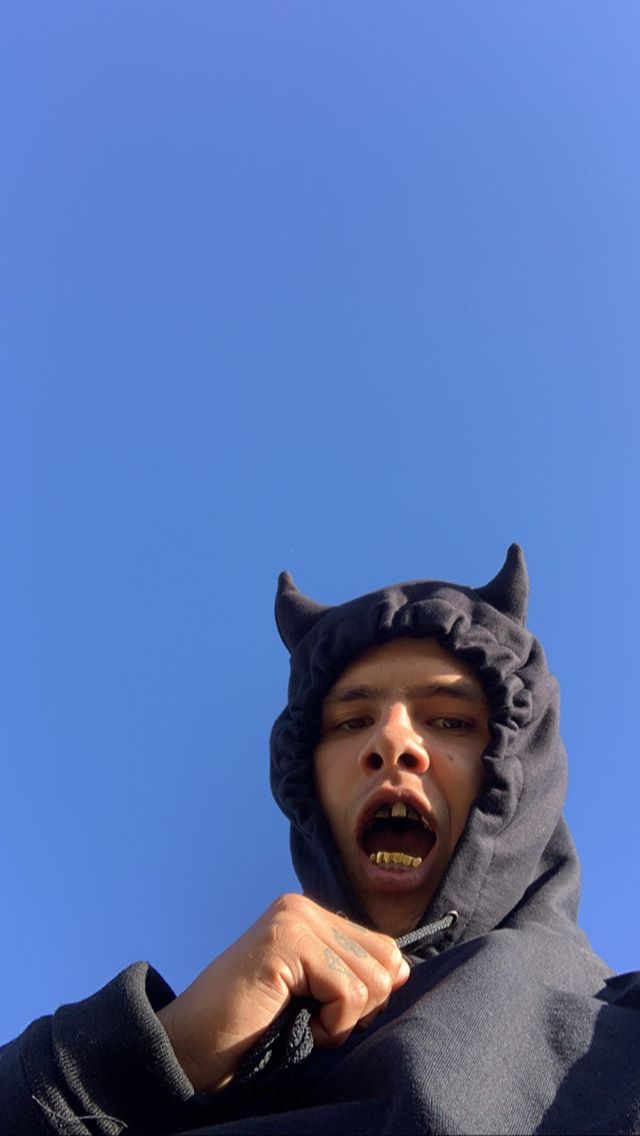 a man wearing a devil costume with his mouth open and tongue out in front of a blue sky