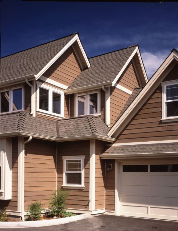 a brown house with white trim and two garages on each side, in front of a blue sky