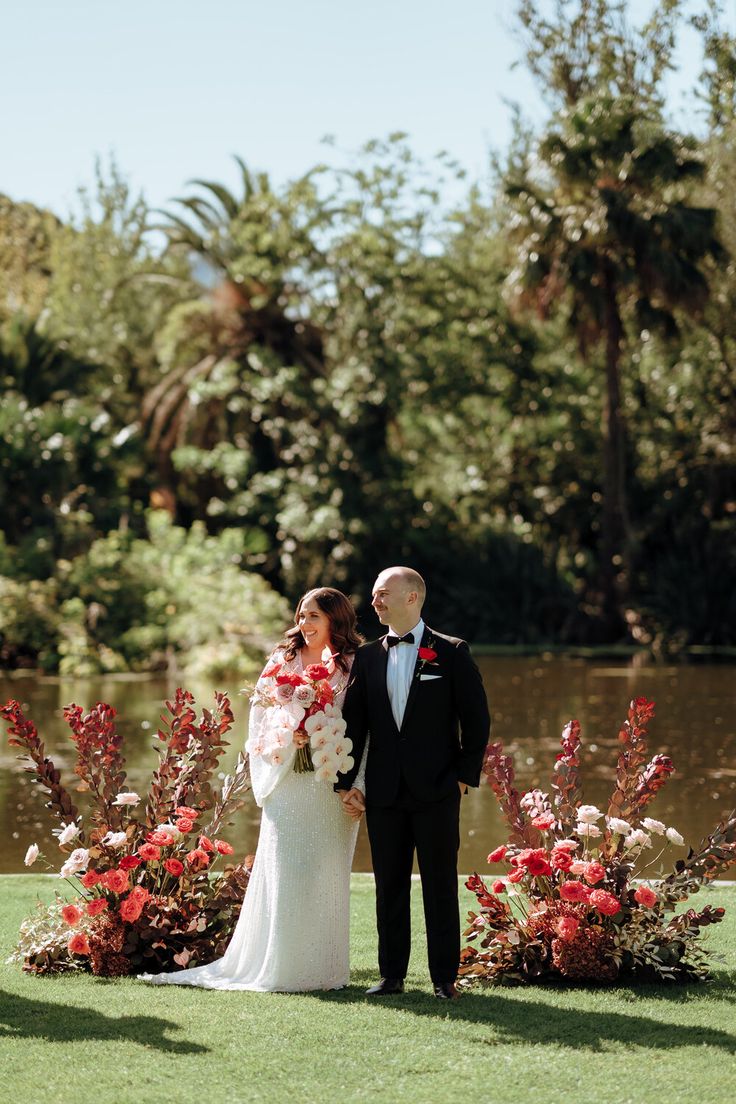 a bride and groom standing next to each other in front of flowers on the grass