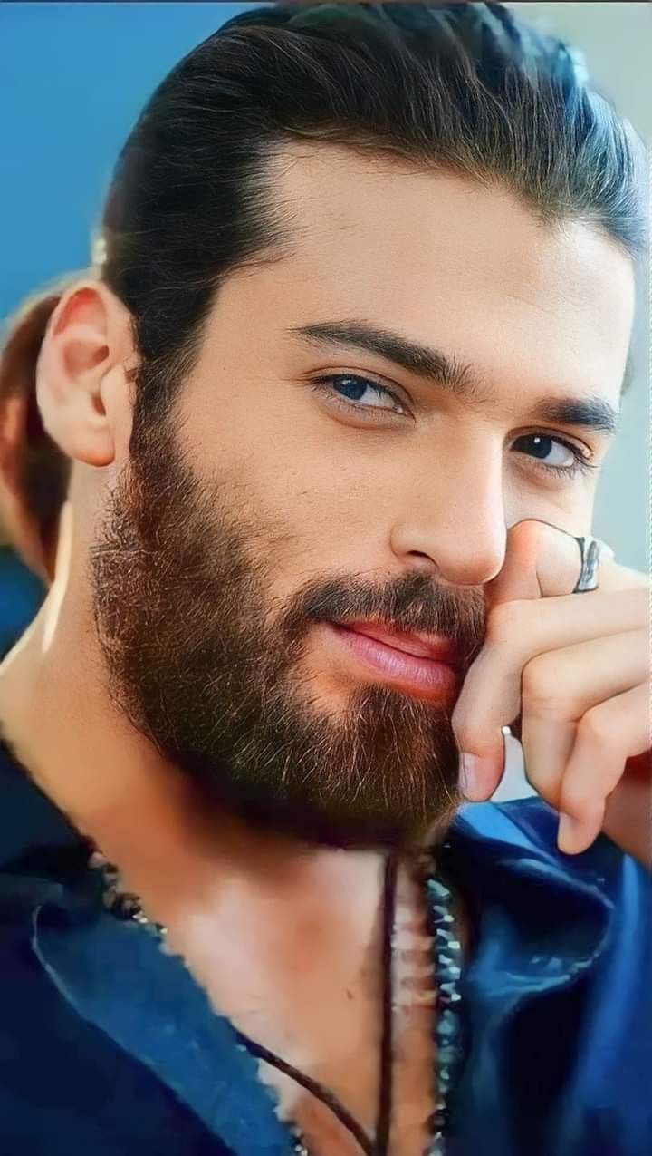 a close up of a person with a beard and ring on his finger, wearing a blue shirt