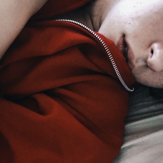 a man laying on top of a bed wearing a red shirt next to his head