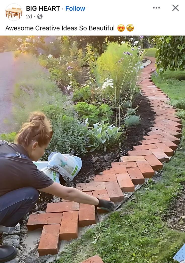 a woman kneeling down to pick up bricks from the ground in front of her garden