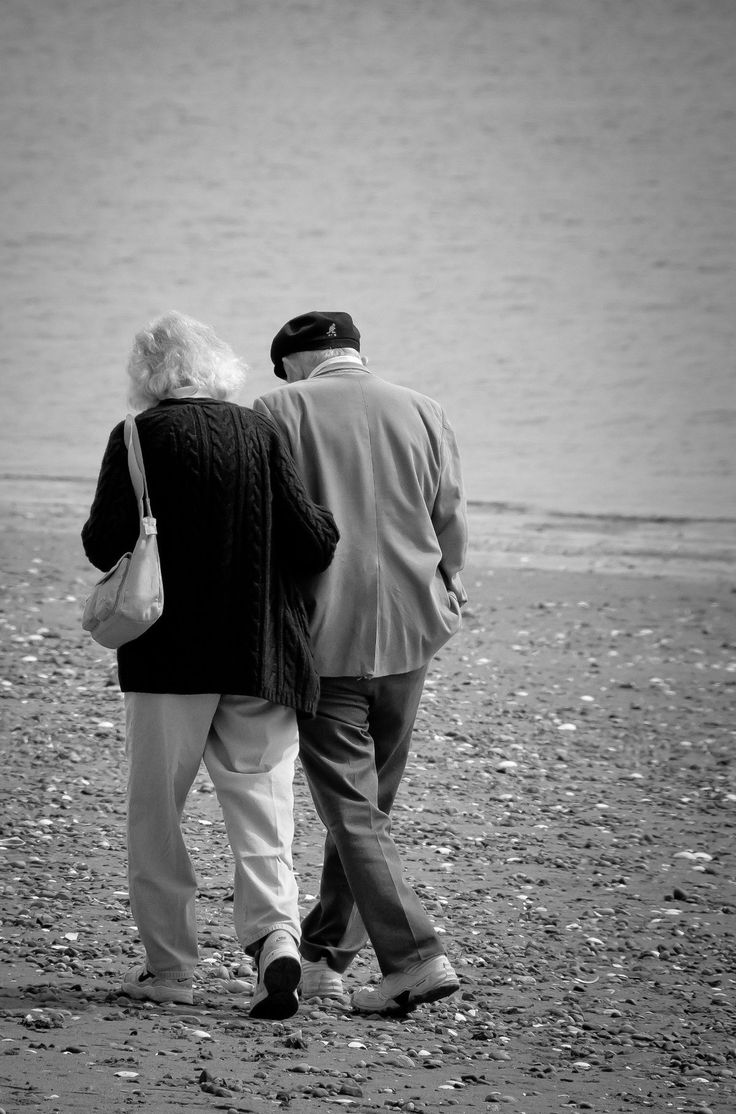 an older couple walking on the beach next to the water looking at the shore line