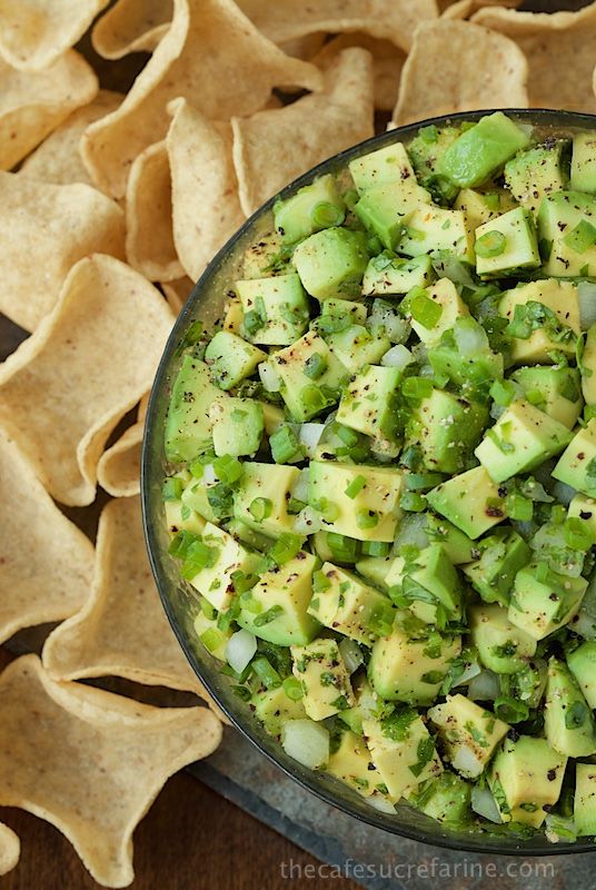 a glass bowl filled with sliced cucumber and tortilla chips on top of a wooden table