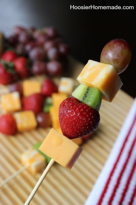 fruit and cheese skewers are arranged on a cutting board