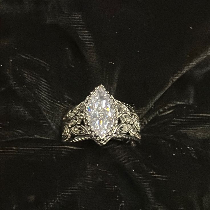 a diamond ring sitting on top of a black velvet cloth covered table with an ornate design