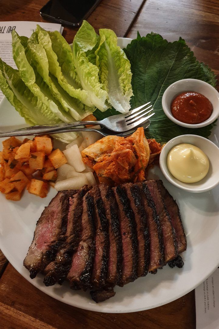 a white plate topped with steak, lettuce and potatoes next to dipping sauce