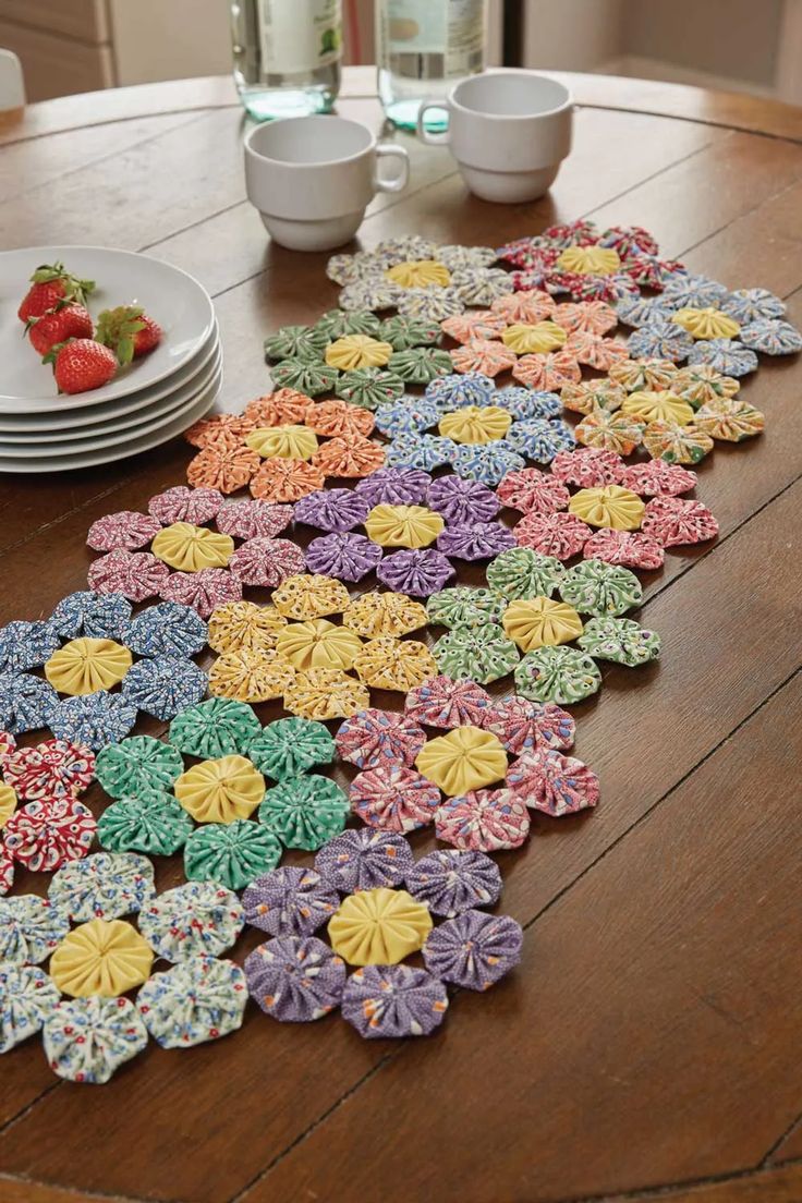 a wooden table topped with lots of colorful crochet doily next to plates and bowls