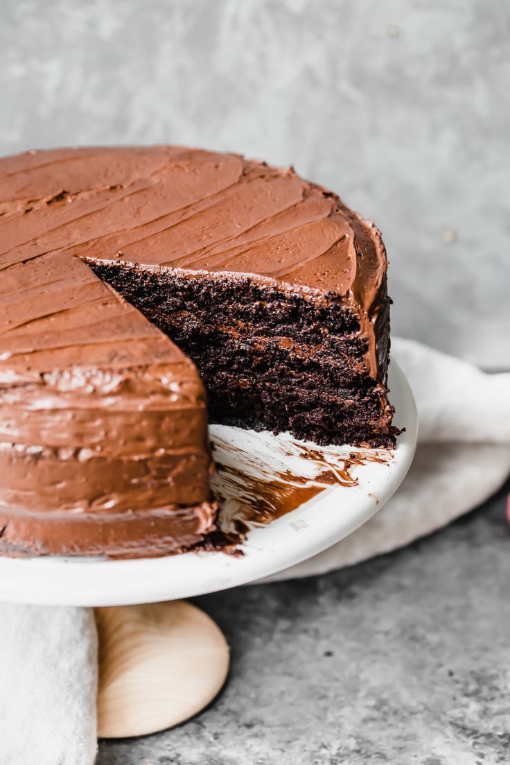 a chocolate cake with one slice taken out of it on a white plate and someone is holding the rest of the cake