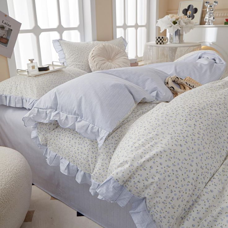 a bed with white sheets and blue ruffles on the bottom, along with pillows