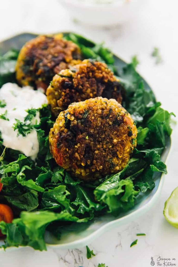 three falafes on a plate with lettuce, tomatoes and sour cream