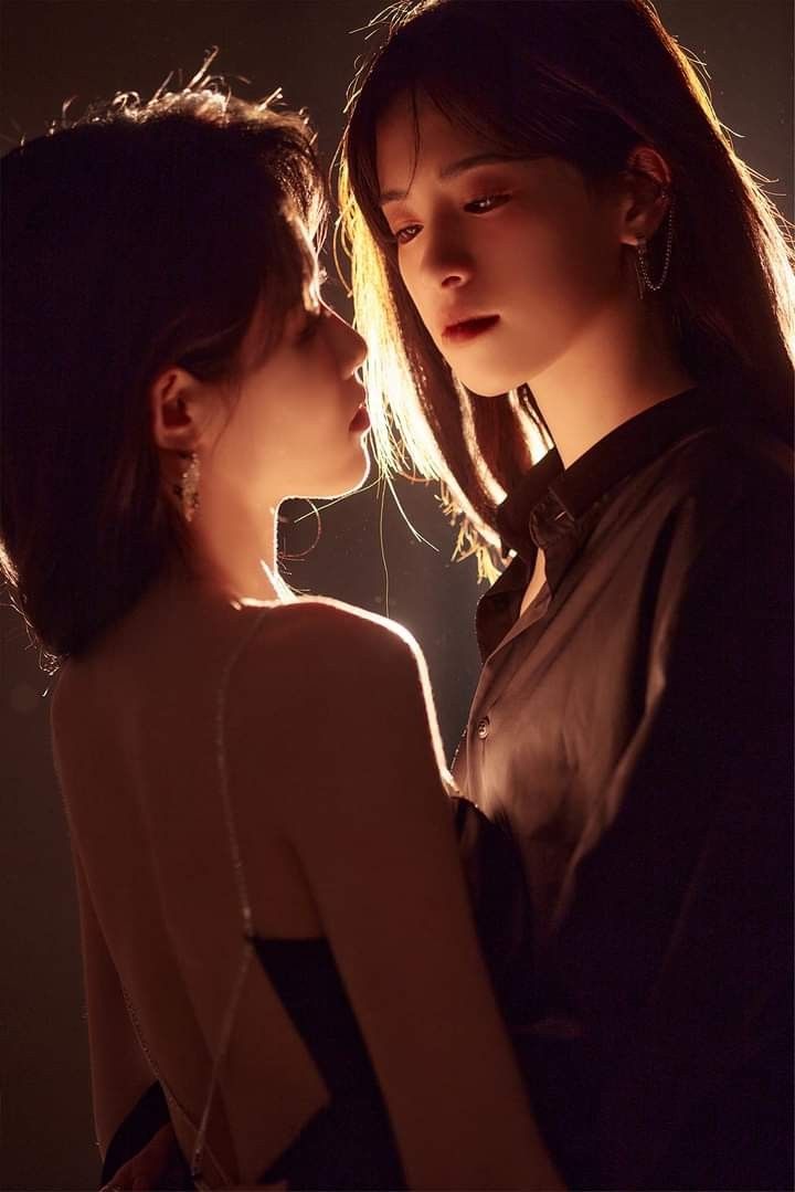 two young women standing next to each other in front of a dark background with light coming from behind them