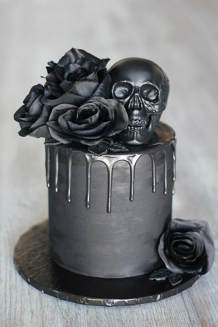 a cake decorated with black icing and roses on a wooden table next to a skull