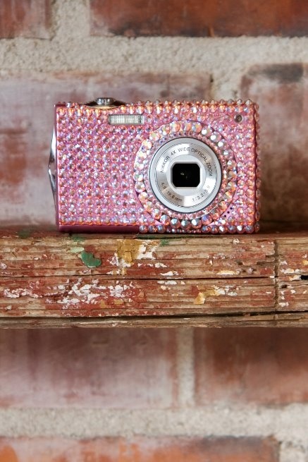 a small pink camera sitting on top of a wooden shelf next to a brick wall